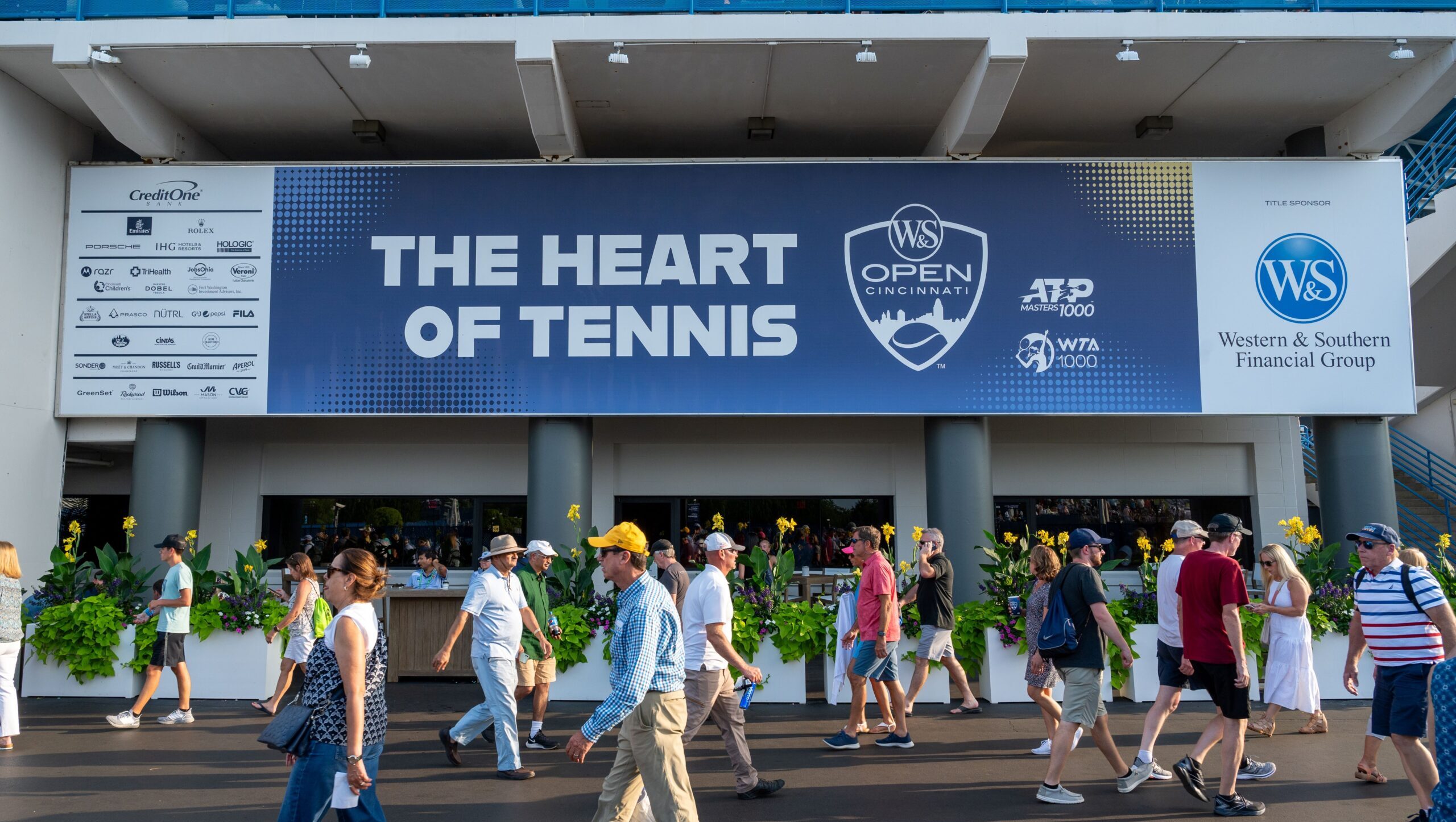 The Heart of Tennis sign with fans walking in front of it